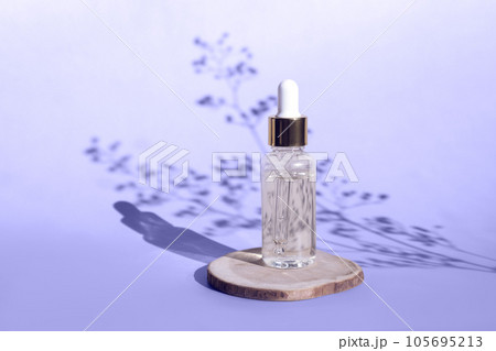 Natural oil cosmetics on violet background. Dropper glass Bottle Mock-Up. Oily cosmetic pipette. Face and body treatment, spa concept. Mineral organic oil. Front view beauty products. Blank bottle 105695213