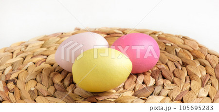 Easter colorful eggs in a basket on white wooden table. Burlap background. Happy Easter. Rustic, Eco concept. Dyed Eggs on a straw Napkin. Easter colorful eggs in a basket on white wooden table. Burlap background. Happy Easter. Rustic, Eco concept. Dyed Eggs on a straw Napkin. 105695283