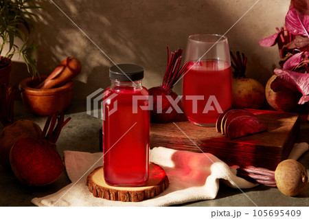 On wooden brown background, unlabeled bottle and glass of beetroot juice decorated with beetroot slices. Classic style for product advertisement with fresh ingredients, beets and vegetables 105695409