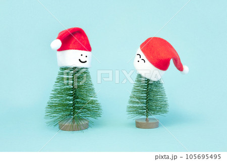 Two small Christmas trees in a red Santa Hats. Decorating of Artificial Fir tree. Beautiful imitation of a mini Christmas tree, with Santa Cap on blue background. Christmas holidays concept Two small Christmas trees in a red Santa Hats. Decorating of Artificial Fir tree. Beautiful imitation of a mini Christmas tree, with Santa Cap on blue background. Christmas holidays concept 105695495