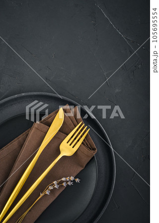 table place setting with black plates and golden cutlery on black  background table place setting with black plates and golden cutlery on black  background 105695554