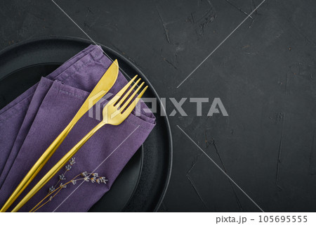 table place setting with black plates and golden cutlery on black background table place setting with black plates and golden cutlery on black background 105695555