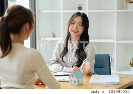 Real estate broker agent presenting and consult to customer to decision making sign insurance form agreement, home model, concerning mortgage loan offer for and house insurance. 105696050