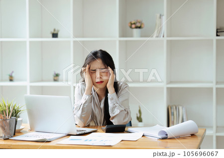 Tired business woman in stress works at a laptop while sitting at a table and holds her hand on her temples, migraine attack. 105696067