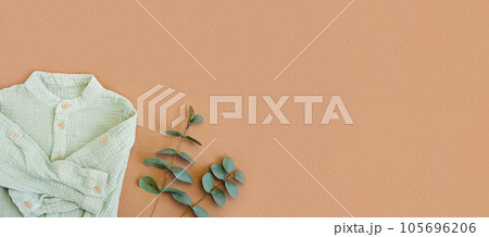 Green baby shirt with eucalyptus on beige background with blank space for text. Baby natural material accessories concept. Top view, flat lay. Baby boy boho wear design. Newborn baby natural material Green baby shirt with eucalyptus on beige background with blank space for text. Baby natural material accessories concept. Top view, flat lay. Baby boy boho wear design. Newborn baby natural material 105696206