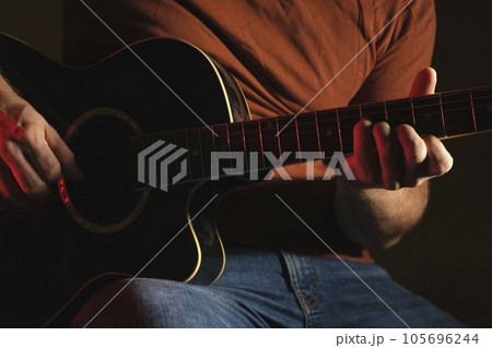 Man Playing Guitar with Neon Light. Unrecognizable Person Rehearsing. Strumming Acoustic Guitar. Musician Plays Music. Male Fingers and Fretboard Close Up. Man Hand Playing Guitar Neck in a Dark. Man Playing Guitar with Neon Light. Unrecognizable Person Rehearsing. Strumming Acoustic Guitar. Musician Plays Music. Male Fingers and Fretboard Close Up. Man Hand Playing Guitar Neck in a Dark. 105696244