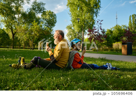 Tired and happy grandfather and grandson having ice-cream after roller skating 105696406