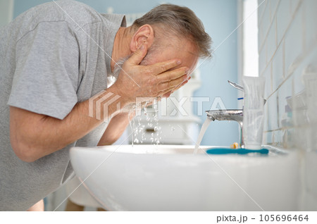 Senior man washing face at sink in home bathroom 105696464