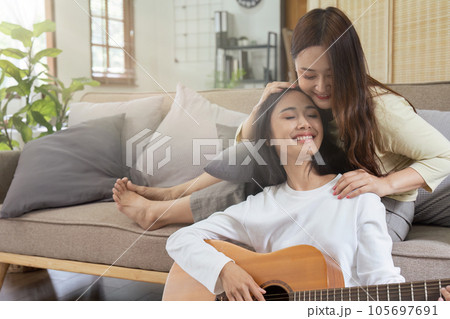 LGBTQIA lesbian gay couple playing guitar and singing with romantic feelings at home LGBTQIA lesbian gay couple playing guitar and singing with romantic feelings at home 105697691