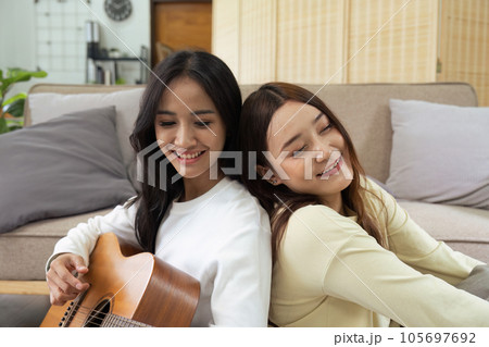 LGBTQIA lesbian gay couple playing guitar and singing with romantic feelings at home LGBTQIA lesbian gay couple playing guitar and singing with romantic feelings at home 105697692