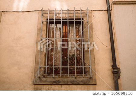 Antique old window with black iron bars framed on a light yellow wall. Pisa, Italy 105699216