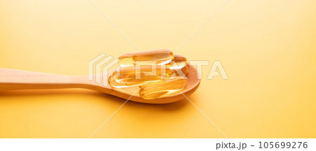 Oil softgel capsules in wooden spoon on yellow background. Nutritional supplement contains fish oil, omega 3, omega 6, omega 9, vitamin e, vitamin d and vitamin a. 105699276