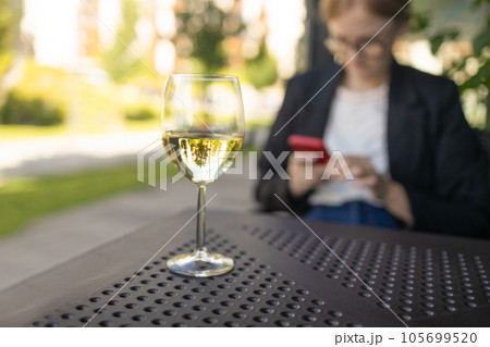 Aesthetic glass of white wine or water with blurry city cafe background. Elegant blonde lady with glass of red wine in restaurant 105699520