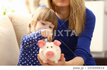 Child little girl arm putting coins into piggybank 105699918