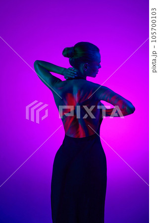 Back view. Tender relaxing woman in digital neon filter lights showing red flower on back over gradient purple background. Back view. Tender relaxing woman in digital neon filter lights showing red flower on back over gradient purple background. 105700103
