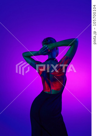 Blossom lady. Young sensual woman in digital neon filter lights showing red flower on back over gradient purple background. 105700104