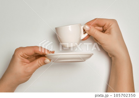 Female hands holding a white coffee cup and saucer on a white background, concept Female hands holding a white coffee cup and saucer on a white background, concept 105702350