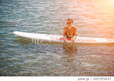Woman sup sea travel. Sports girl on a surfboard in the sea on a sunny summer day. In a black bathing suit, he sits on a sapa in the sea. Rest on the sea. Woman sup sea travel. Sports girl on a surfboard in the sea on a sunny summer day. In a black bathing suit, he sits on a sapa in the sea. Rest on the sea. 105705637