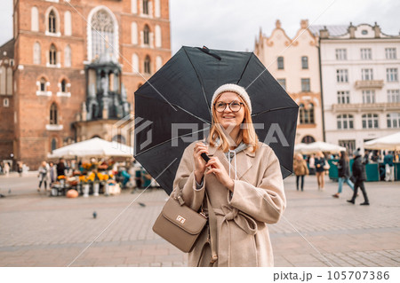 Young blonde woman smiles under a black umbrella breathing in the street of and old town Krakow in a rainy day. High quality photo. Natural beauty Young blonde woman smiles under a black umbrella breathing in the street of and old town Krakow in a rainy day. High quality photo. Natural beauty 105707386
