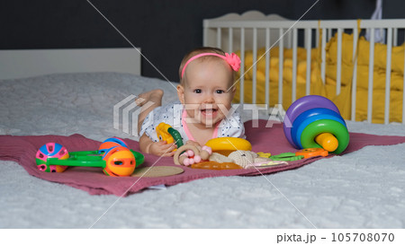 Smiling baby girl playing with teething toy while lying on tummy on bed at home 105708070