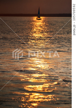 The view of sailboat is heeling at sunset, reflection of sun on water surface The view of sailboat is heeling at sunset, reflection of sun on water surface 105709592