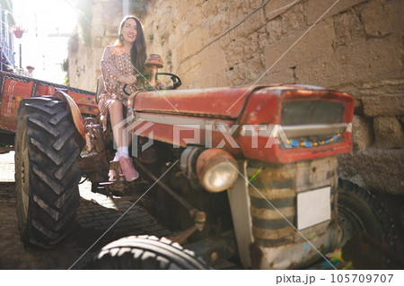 A beautiful girl in a dress rides an old tractor A beautiful girl in a dress rides an old tractor 105709707