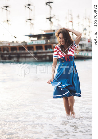 a beautiful sexy girl in a sea uniform walks on the beach against the background of ships. a beautiful sexy girl in a sea uniform walks on the beach against the background of ships. 105709982