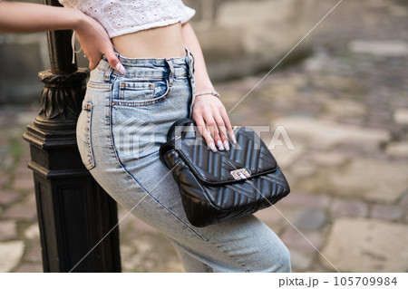 a close-up of the waist of a girl in fashionable clothes and a handbag in her hands a close-up of the waist of a girl in fashionable clothes and a handbag in her hands 105709984