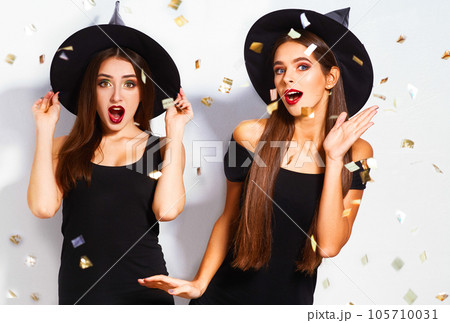 portrait of two happy young women in black witch halloween costumes on party over white background. 105710031