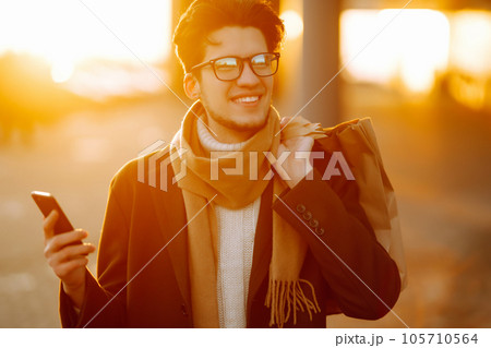 Stylish man with paper packages after shopping at sunset. Handsome man doing shopping. 105710564