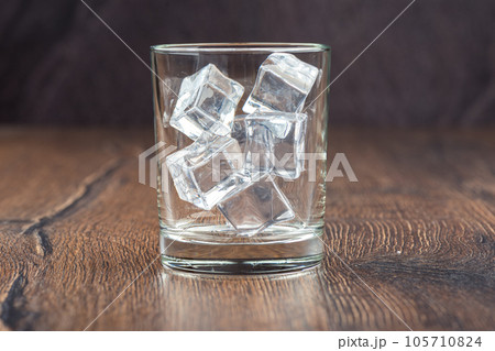 Ice cubes in an empty glass on a wooden bar counter, dark background. 105710824