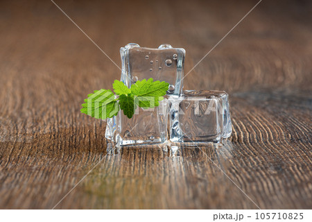 Mint leaves and a melting ice cube with water drops on the table. 105710825