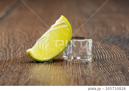 Slice of lime and a melting ice cube with drops of water on the table. 105710826