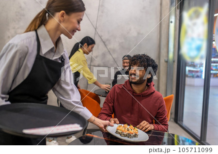 Smiling waitress passing the plate with sushi to the customer at the cafe Smiling waitress passing the plate with sushi to the customer at the cafe 105711099