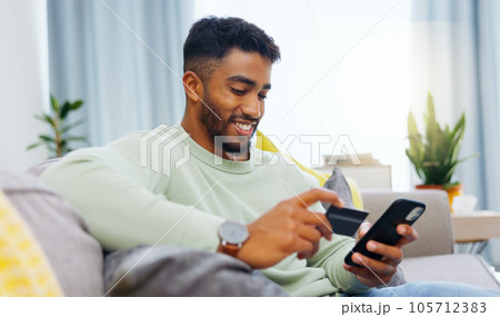 Credit card, finance and man with smartphone for online shopping in lounge at home. Indian, visa and money for e commerce transaction and search the internet for investment or product. 105712383