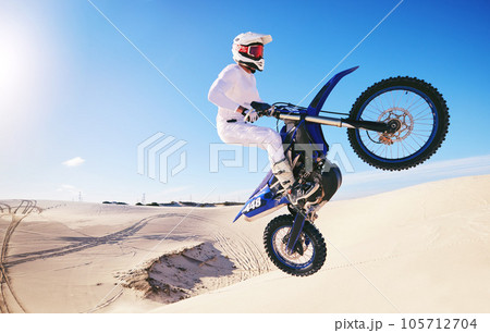 Jump, sports and man on motorcycle on sand for adrenaline, adventure and freedom in desert. Action, extreme motorbike and male person on bike on dunes for training, exercise and race or challenge 105712704
