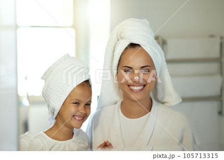 Playful mother and daughter doing a hygiene, skincare routine together in the bathroom. Mom teaching her adorable child a grooming and beauty treatment regime. Parent and little girl applying lotion 105713315