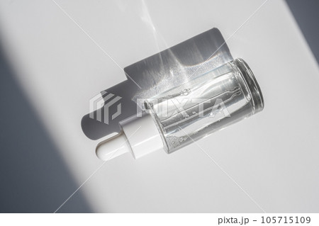 A white transparent bottle with serum in the rays of the sun. 105715109