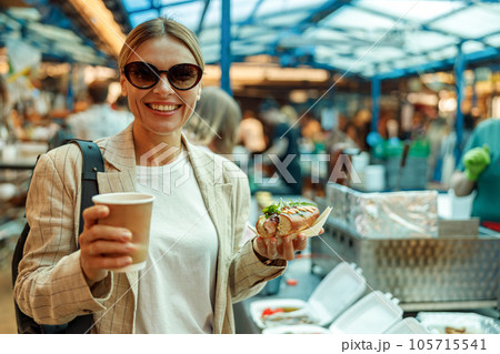 Smiling mature woman is having a takeaway fast food lunch on food market and drink coffee  105715541