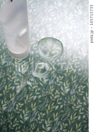 A transparent bottle of cosmetic gel on a green background with drops of the product. A transparent bottle of cosmetic gel on a green background with drops of the product. 105715735