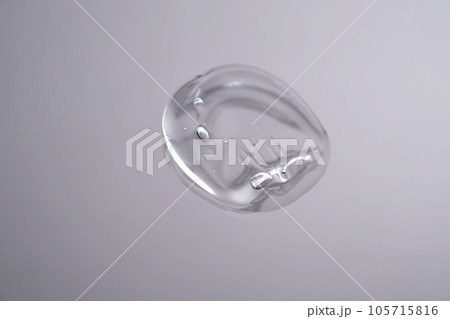 Drop of cosmetic transparent gel on a grey background. The texture of the serum, heir gel or hyaluronic booster. Drop of cosmetic transparent gel on a grey background. The texture of the serum, heir gel or hyaluronic booster. 105715816