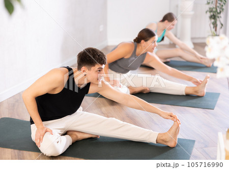 Yoga class of sports women and man performing Head to Knee Forward Bend Pose, or Janu Sirsasana after practicing together 105716990
