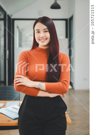 Portrait of young smiling woman looking at camera with crossed arms. Happy girl standing in creative office. Successful businesswoman standing in office with copy space. 105721515