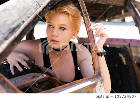 glamorous girl in pants and short hair and makeup posing near a broken old car. 105724807