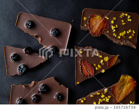 Dark chocolate broken with blueberries on a black background. View from above. Dark chocolate broken with blueberries on a black background. View from above. 105726739