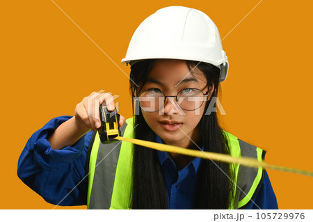Portrait of Asian girl posing as an engineer or architect on yellow background. Dream occupation, future profession and learning concept Portrait of Asian girl posing as an engineer or architect on yellow background. Dream occupation, future profession and learning concept 105729976