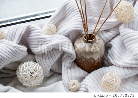 Aroma reed diffuser. Bottle container with wood stick diffusers Essential oils to scent your home fragnance concept autumn holidays at cozy home on the windowsill Hygge aesthetic atmosphere on knitted 105730575