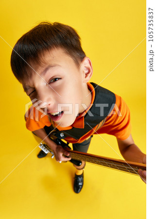 Meme face. Boy, child in stylish clothes playing guitar against yellow studio background. Music lifestyle and education 105735837