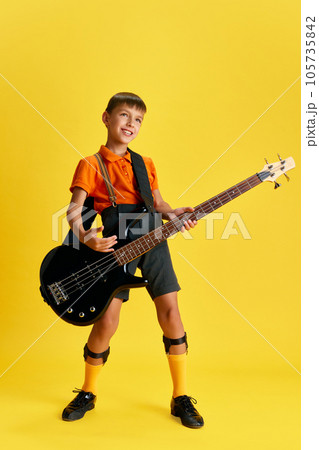 Boy, child in stylish clothes playing guitar against yellow studio background. Music and education Boy, child in stylish clothes playing guitar against yellow studio background. Music and education 105735842
