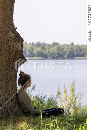 Enchanted Dreams: Young Woman Gazing at the Forest Lake from Beneath a Tree Enchanted Dreams: Young Woman Gazing at the Forest Lake from Beneath a Tree 105737626